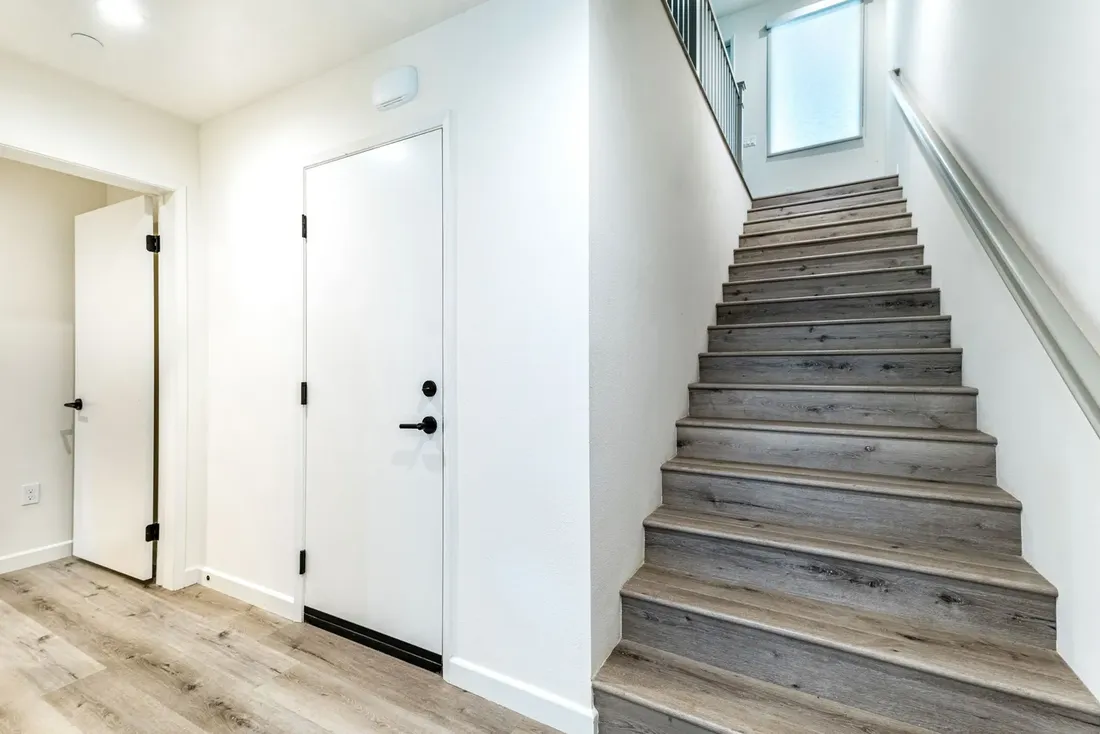 Escalier droit gris avec une main courante fixée au mur, dans l'entrée d'une maison récente