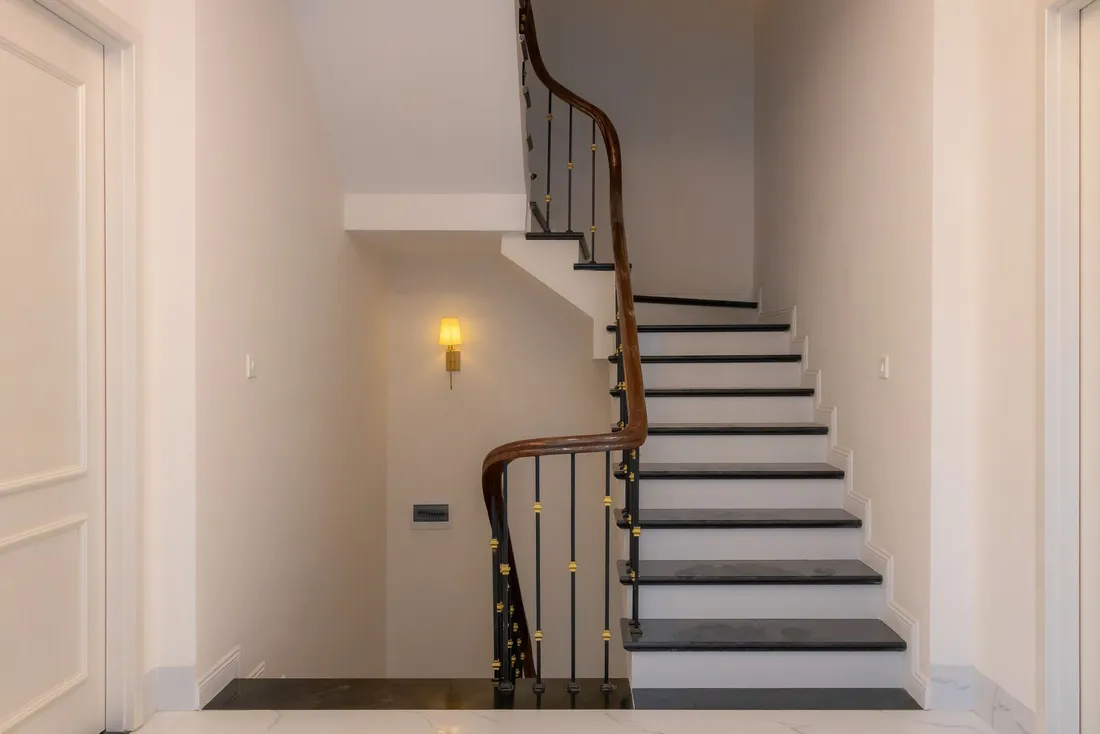 Escalier tournant blanc à rampe en fer forgé dans un hall clair