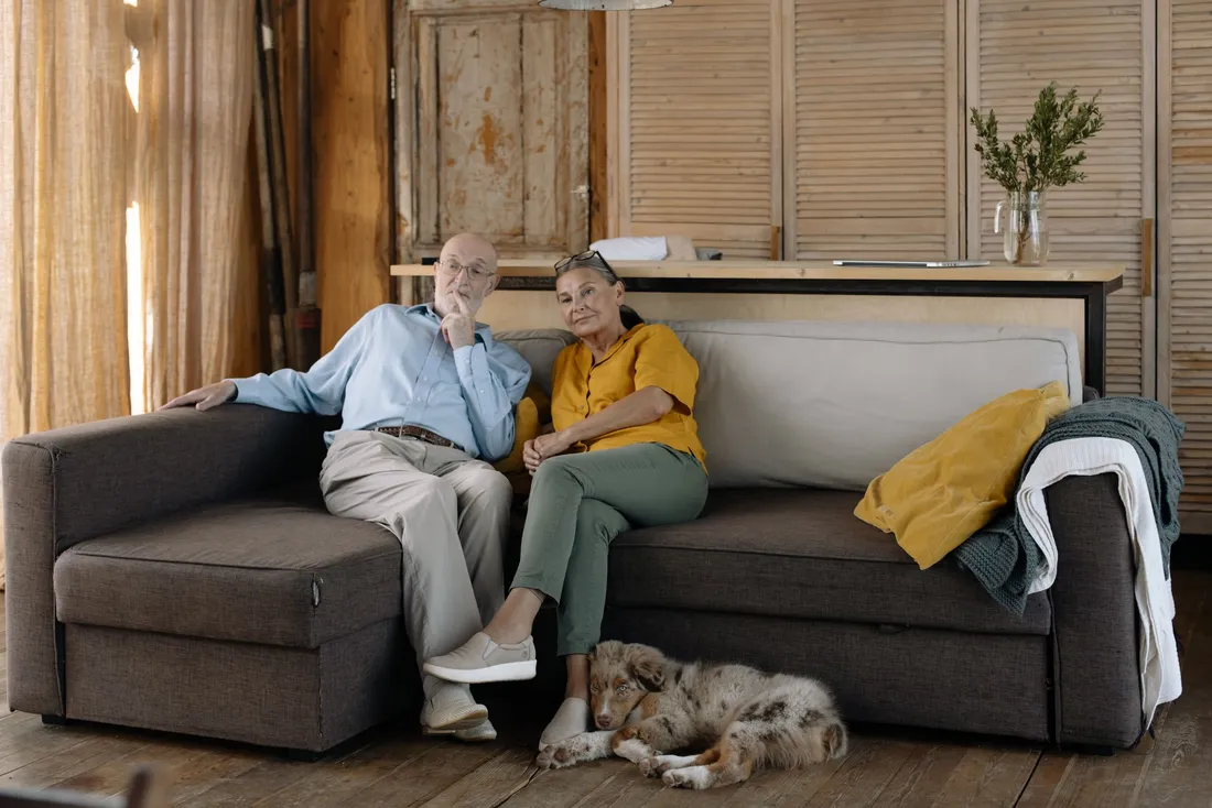 Couple de seniors assis sur le canapé du salon, un chien couché à leurs pieds