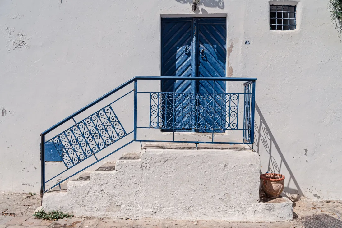 Escalier extérieur maçonné à rampe bleue devant une maison blanche