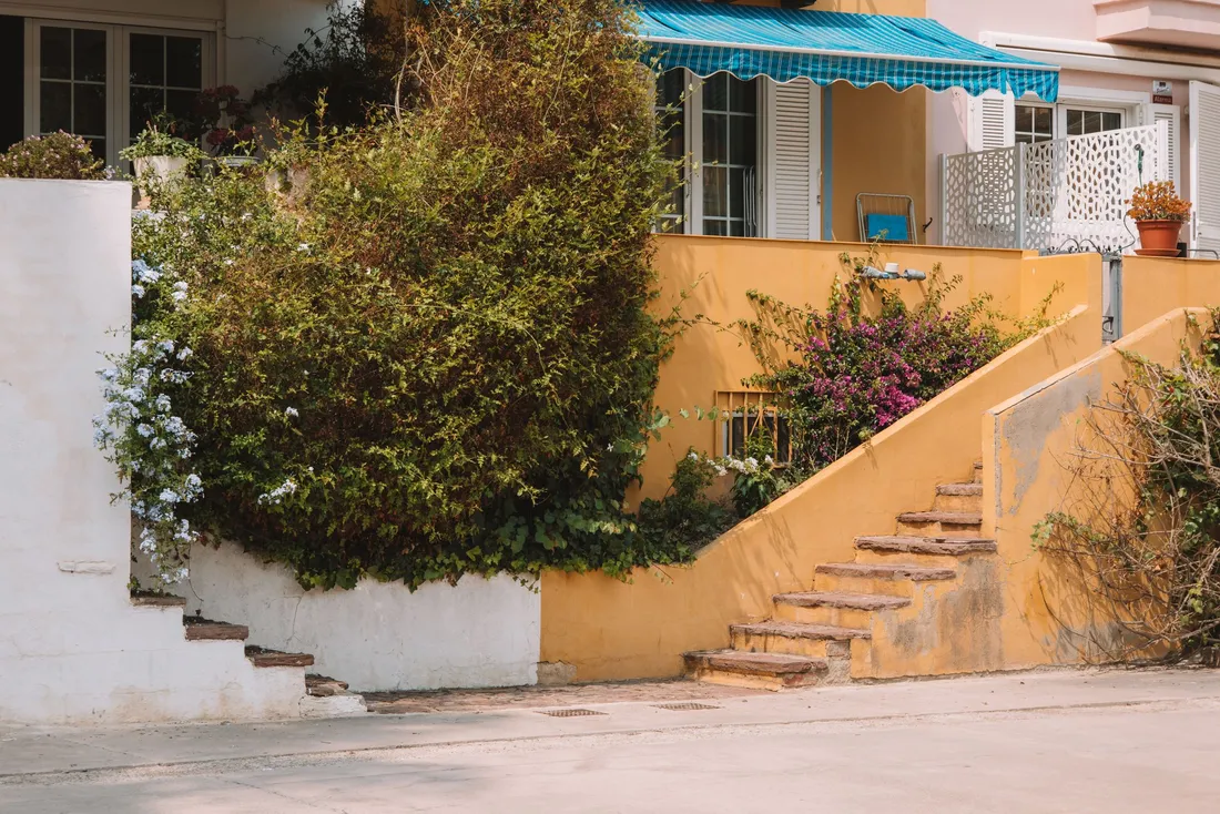 Maison aux murs jaunes avec un escalier extérieur et un jardin fleuri