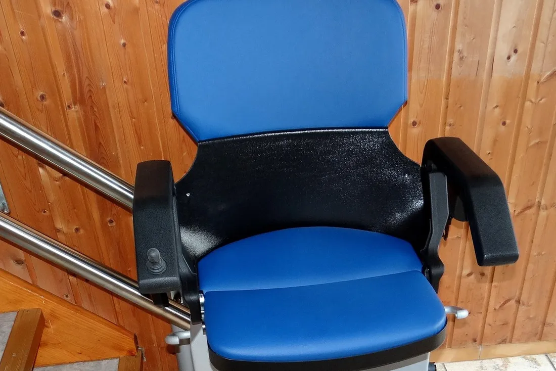 Siège bleu de monte-escalier électrique, manette de commande sur l'accoudoir, devant un rail en inox et un escalier en bois
